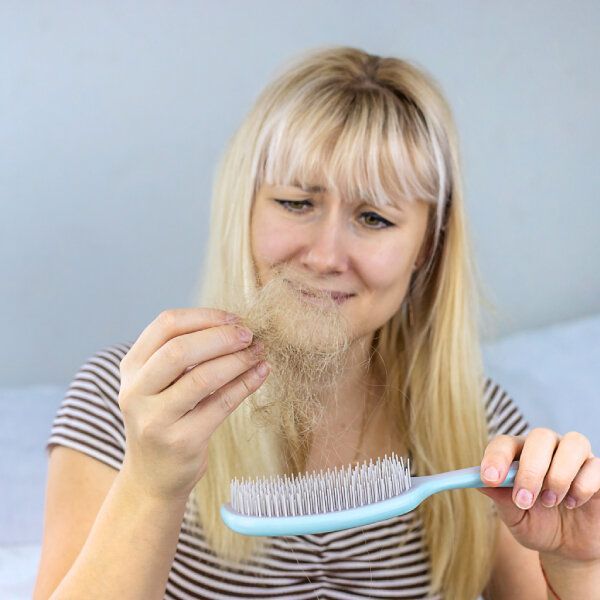 Une femme regarde ses cheveux qui tombent accrochés à sa brosse.
