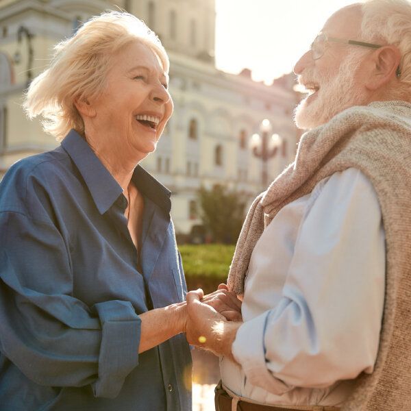 Un couple de seniors souriant en extérieur se tiennent la main.