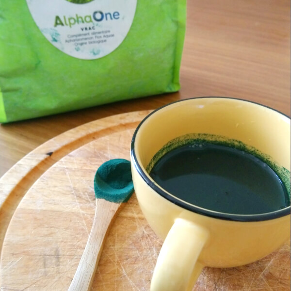 Une tasse remplie d'algue de Klamath Alpha ONE, une petite cuillère en bois remplie d'algue en poudre.