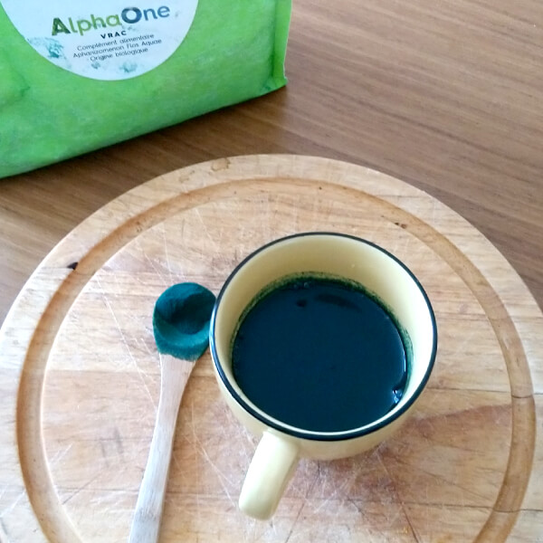 Une tasse remplie d'algue de Klamath Alpha ONE, une petite cuillère en bois remplie d'algue en poudre.