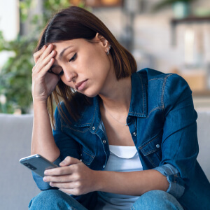 Une femme se prend la tête en regardant son smartphone.