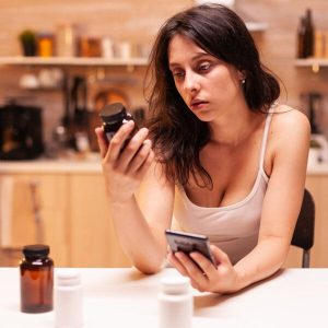 Une femme épuisée lit les mentions d'un flacon de médicaments.