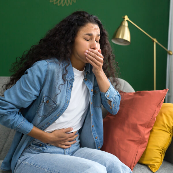 Une jeune femme se tient le ventre et la bouche.