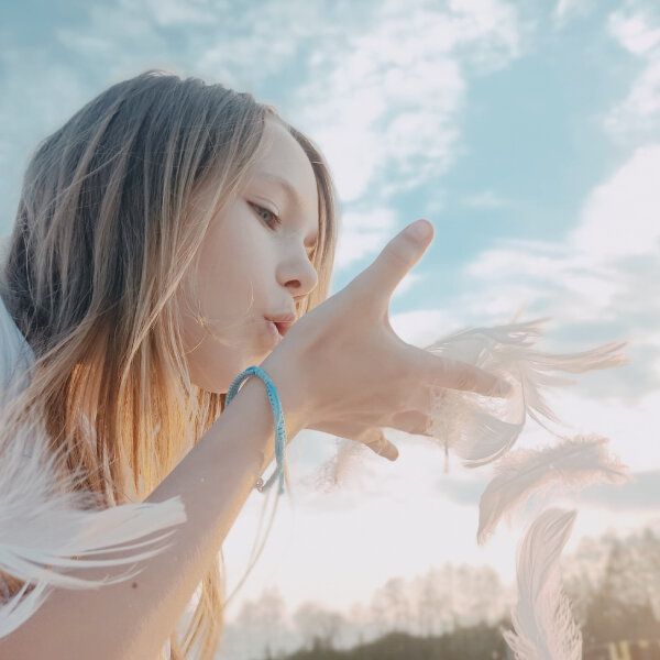 Une petite fille souffle sur des plumes blanches.