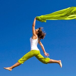 Une femme saute avec un foulard vert contre un ciel bleu.