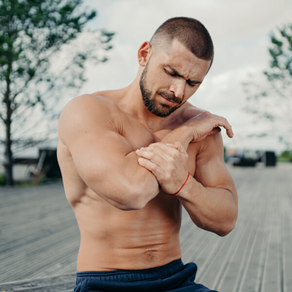 Un jeune homme musclé se tient le coude de douleur.