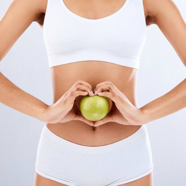 Une femme en sous-vêtements blancs tient une pomme verte devant son estomac.