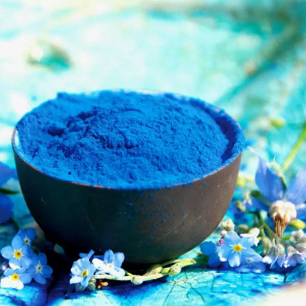 Un bol rempli de phycocyanine bleue avec des fleurs à coté.