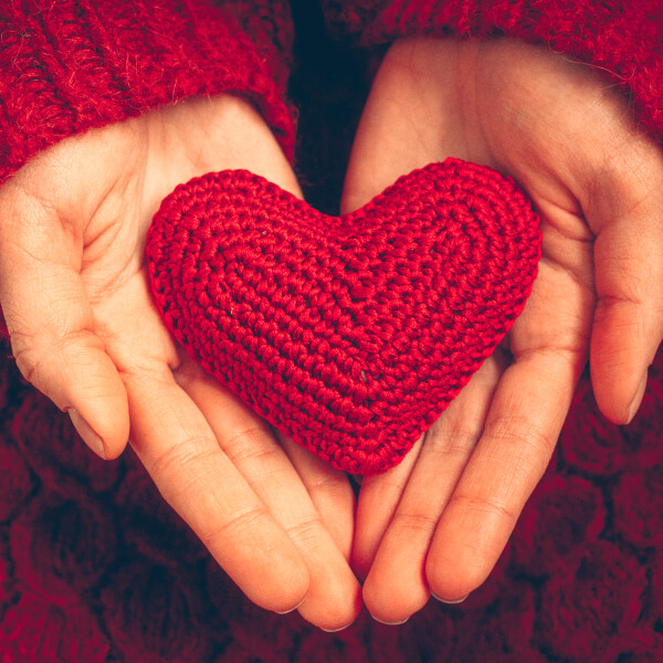 Un coeur en laine rouge tenu entre deux mains.