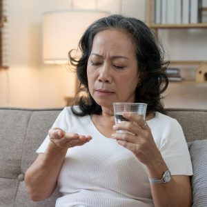 Une dame observe pensivement les médicaments anticoagulants qu'elle s'apprête à avaler avec un verre d'eau.