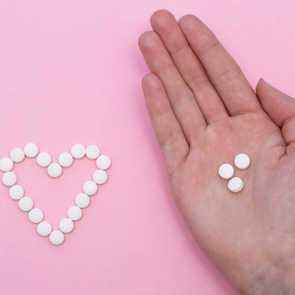 Une main avec des cachets, un coeur dessiné avec des médicaments à coté.