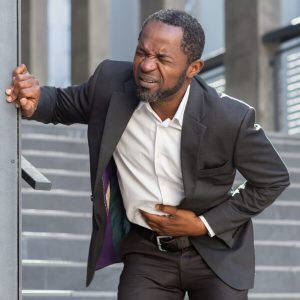 Un homme en costume d'affaire se tient le ventre de douleur suite à des troubles digestifs liés au stress.