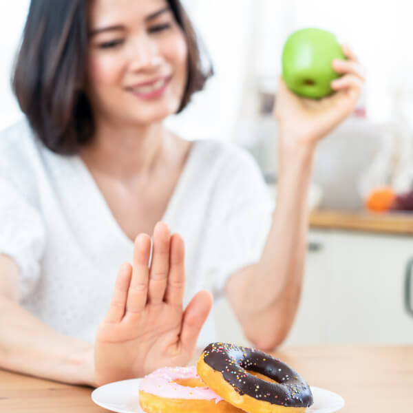 Une jeune femme refuse des donuts sucrés et préfère une pomme verte pour la santé de ses intestins.