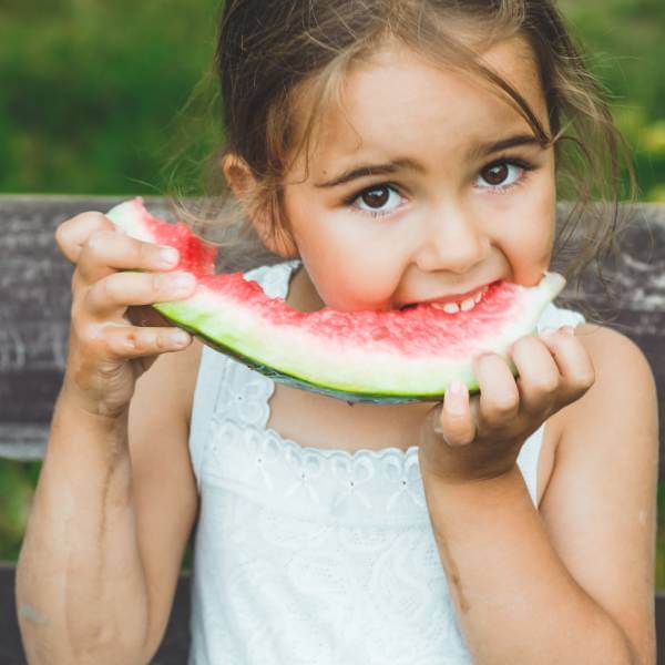 Une petite fille croque dans une pastèque crue.