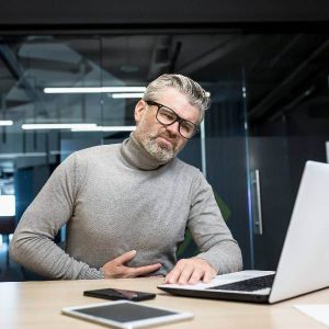 Un homme devant son ordinateur se prends le ventre après avoir mangé des aliments qui fermentent dans l'intestin.