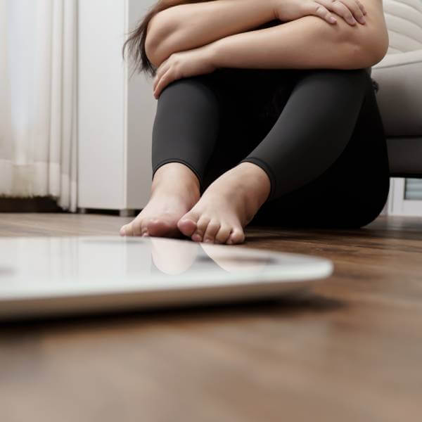 Une femme ayant pris du poids déprime assise devant sa balance à peser.