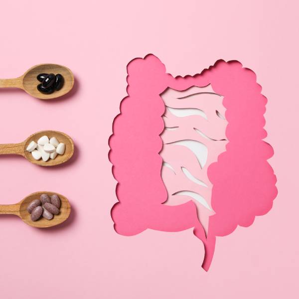 Trois cuillères en bois avec des gélules d'enzymes digestives à coté d'un intestin en papier rose.
