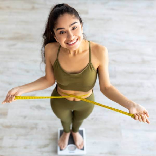 Une jeune femme vue en contre-plongée sur une balance se mesure la taille pour perdre du poids.