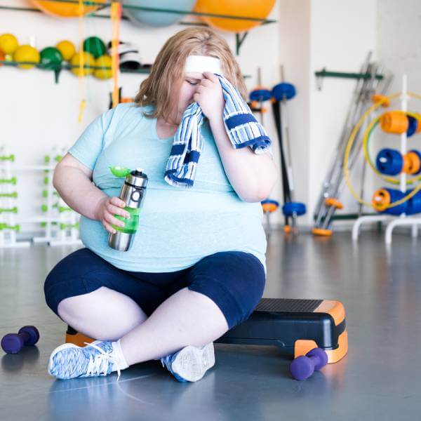 Une jeune femme obèse expérimente une prise de poids, ventre gonflé, fatigue, à la gym.