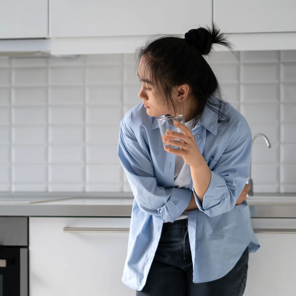 Une jeune femme avec un verre d'eau se plie sous la douleur de l'intestin irritable.