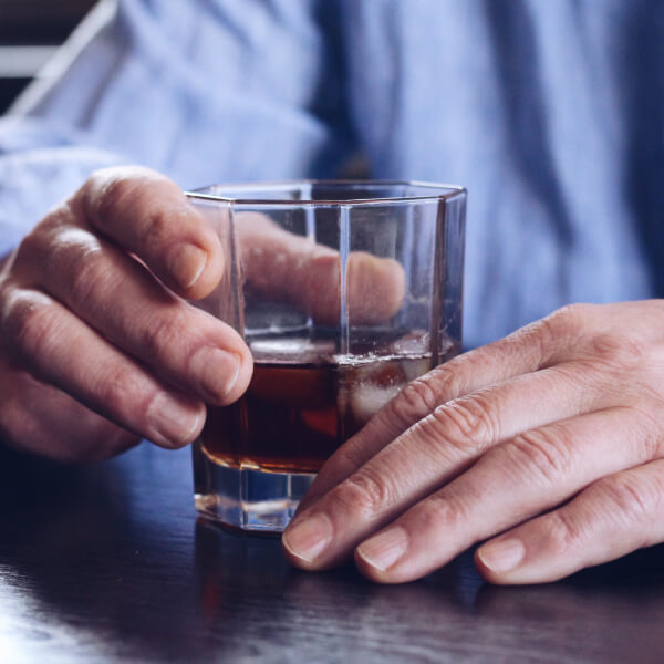 Un verre d'alcool fort tenu par deux mains d'homme.