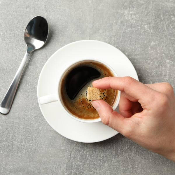 Une main plonge un carré de sucre dans une tasse de café.
