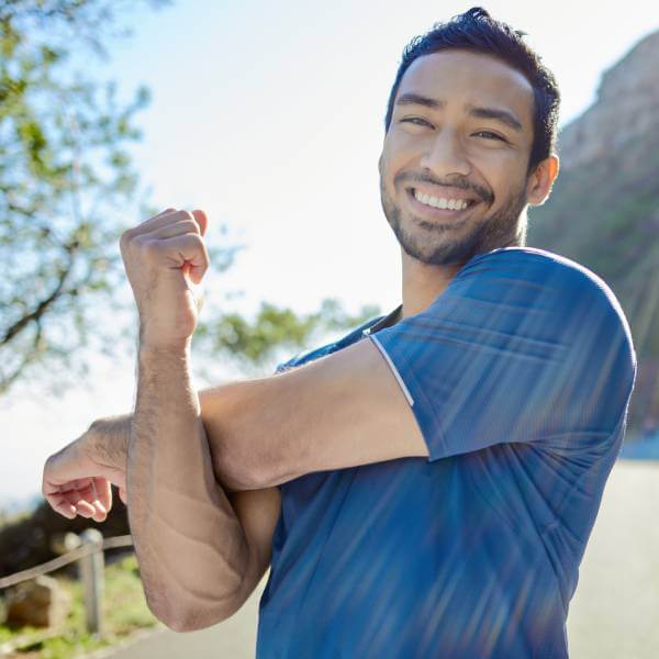 Un jeune homme sportif souriant étire son épaule.