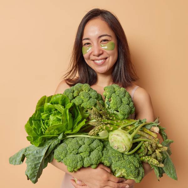 Une jeune femme souriante tient des légumes verts dans ses bras.