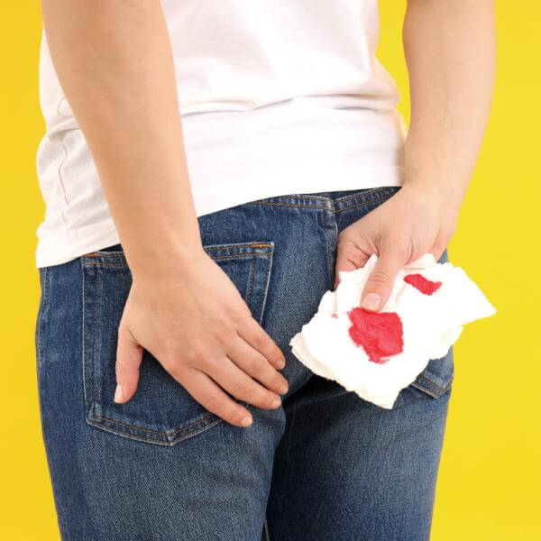 Vue de dos une femme tient un papier toilette imbibé de sang près de ses fesses.