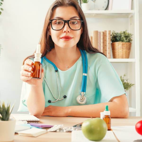 Une docteur médecin souriante dans son cabinet présente un flacon.