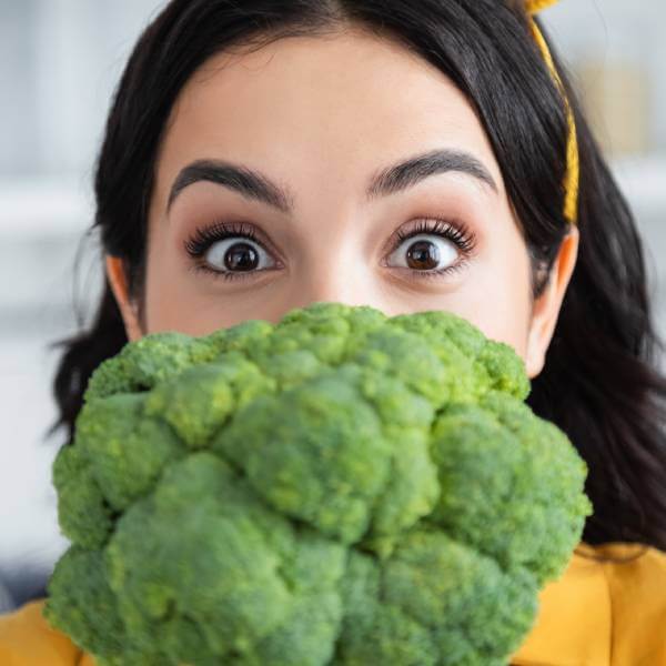 Une jeune femme derrière un gros broccoli.