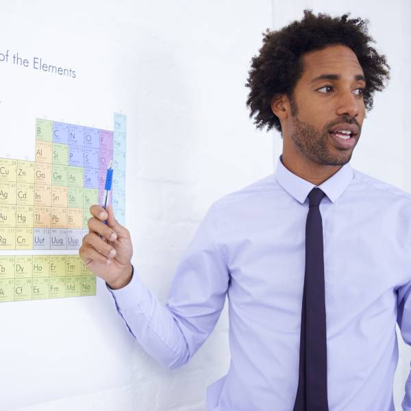 Un professeur de science pointe sur une table périodique la liste des métaux lourds.