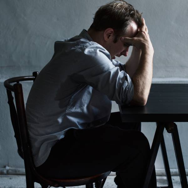 Un homme déprimé se prends la tête assis sur une table, un effet secondaire d'une détox de métaux lourds.