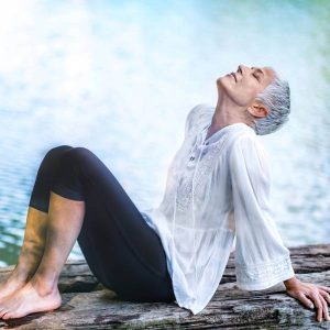Une dame dans la soixantaine se repose et respire profondément près de l'eau.