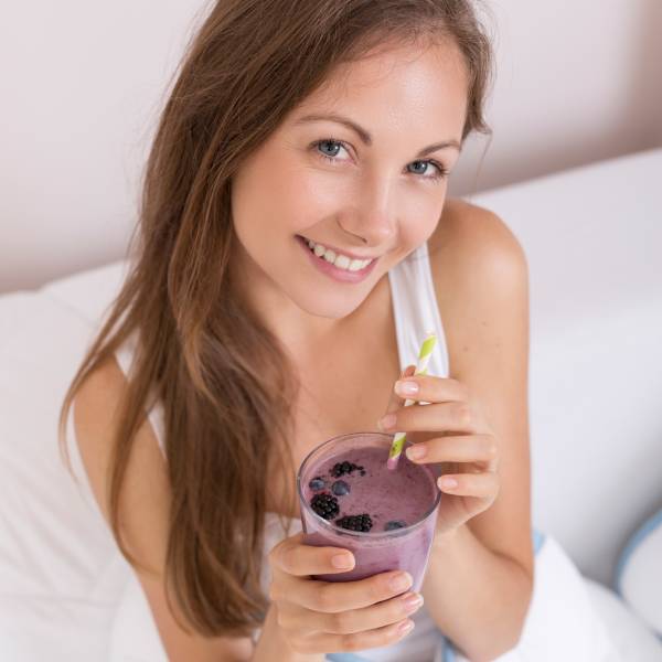 Une jeune femme avec un smoothie aux fruits rouges, un des 6 aliments pour rajeunir la peau.