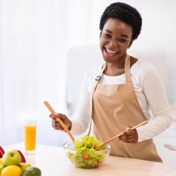 Une femme souriante cuisine avec les 6 meilleurs aliments pour rajeunir la peau.