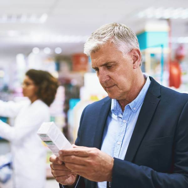 Un monsieur dans une pharmacie regarde un flacon se demandant quels sont les probiotiques les plus efficaces pour l'intestin.