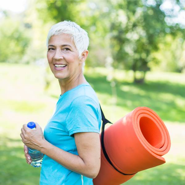 Une dame senior dans la nature avec une bouteille d'eau et un tapis de yoga.