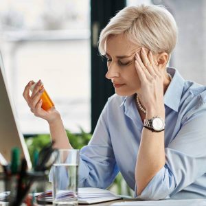Une dame ménopausée regarde un flacon de granules d'homéopathie.