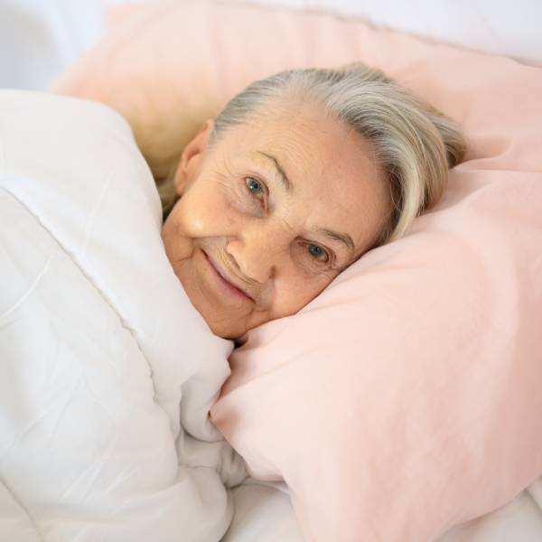Une dame souriante dans son lit bien reposée après avoir bien dormi.