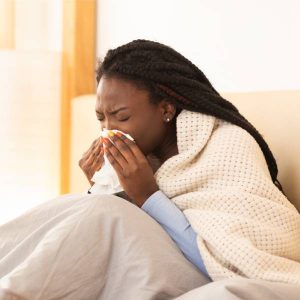 Une jeune femme enrhumée éternue dans un mouchoir.